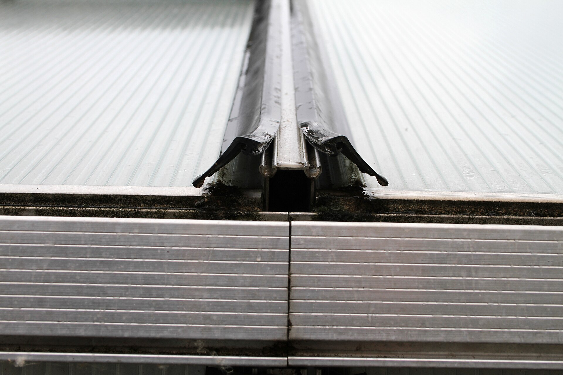 A close-up view of an aluminum greenhouse frame profile with a rubber sealing lip at the panel joint