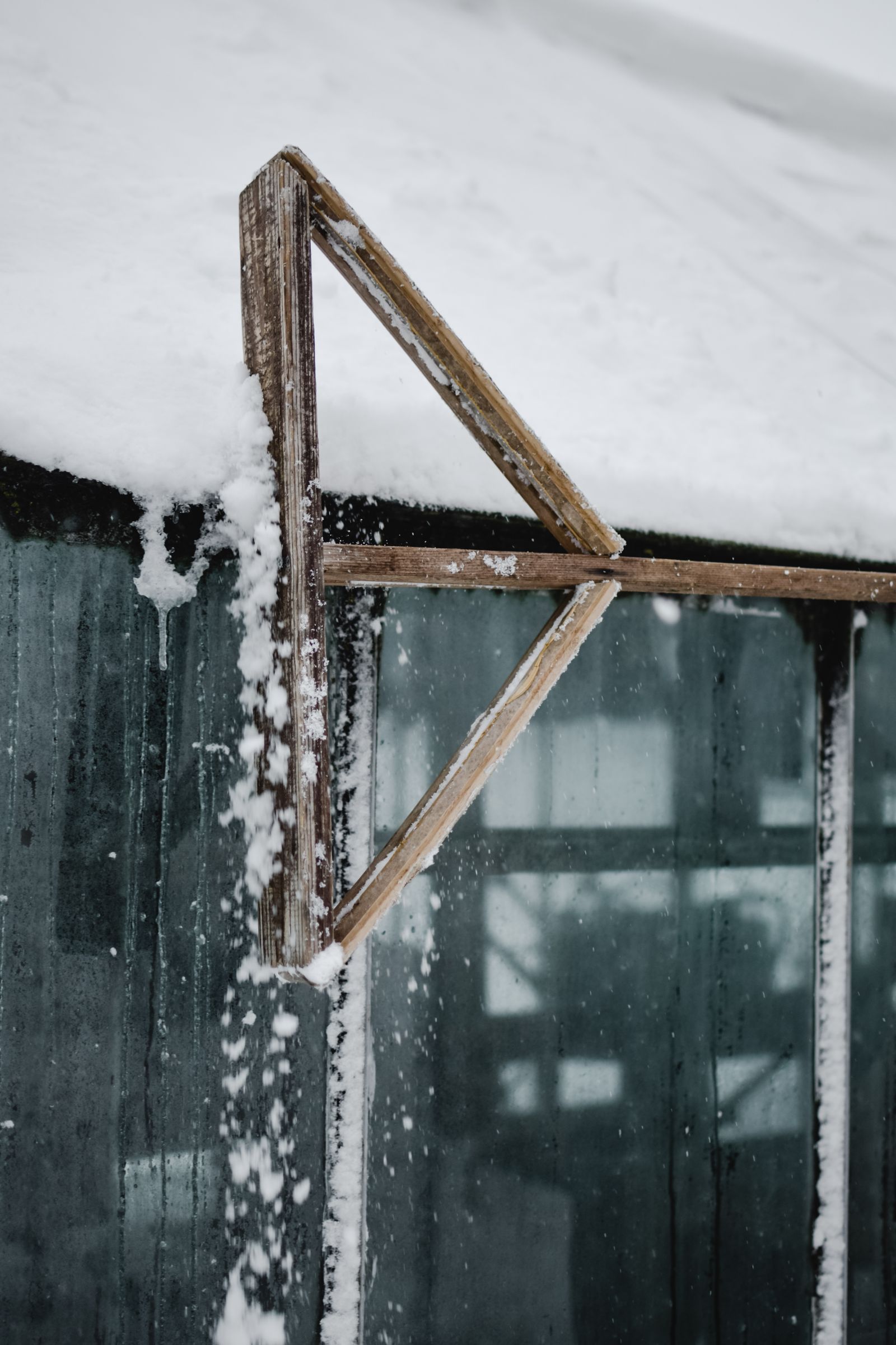 Close-up of snow accumulating on the angled glass panels of a greenhouse roof in winter
