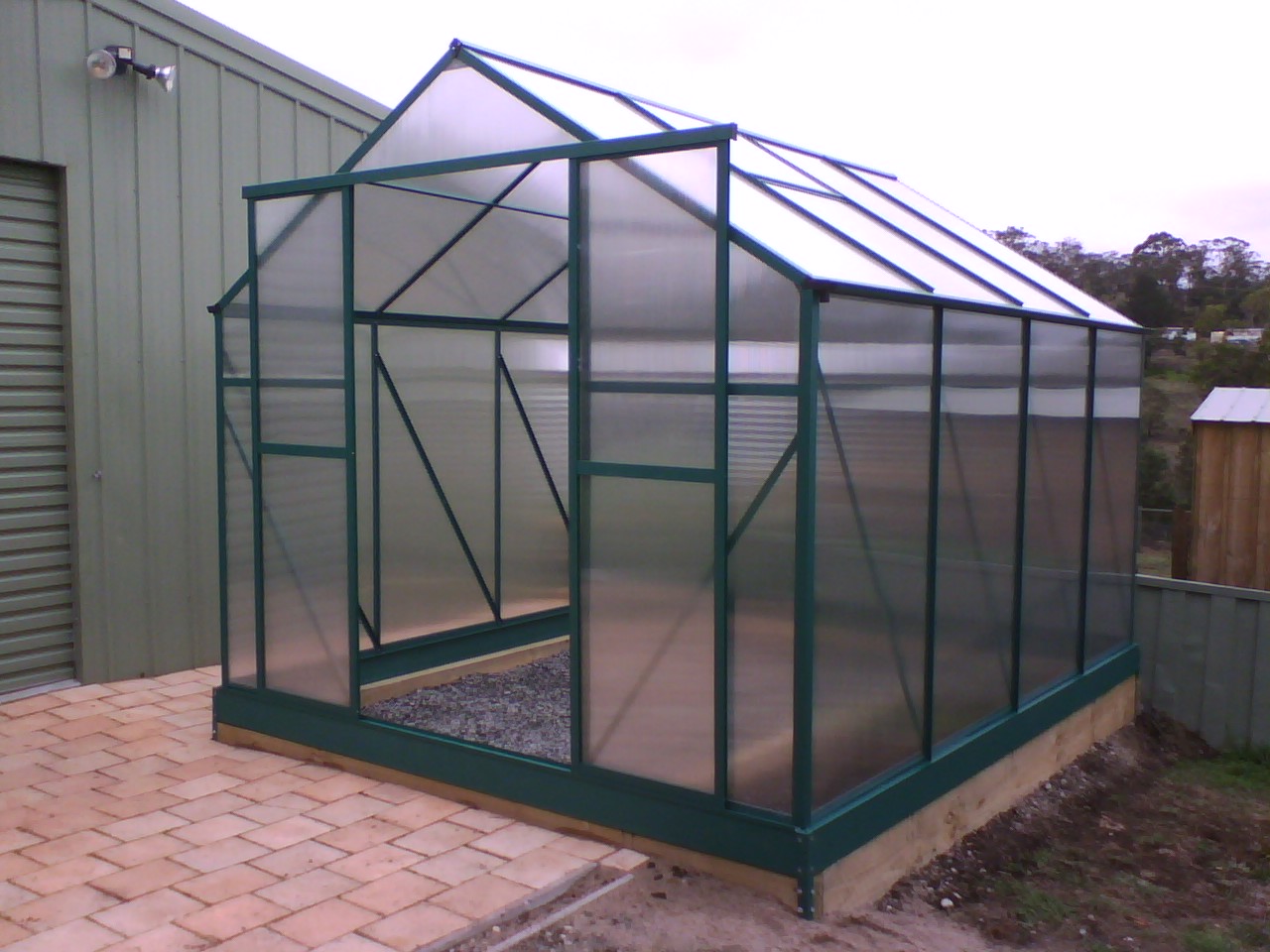 Exterior view of a polycarbonate greenhouse structure with clear twin-wall panels and aluminum framing