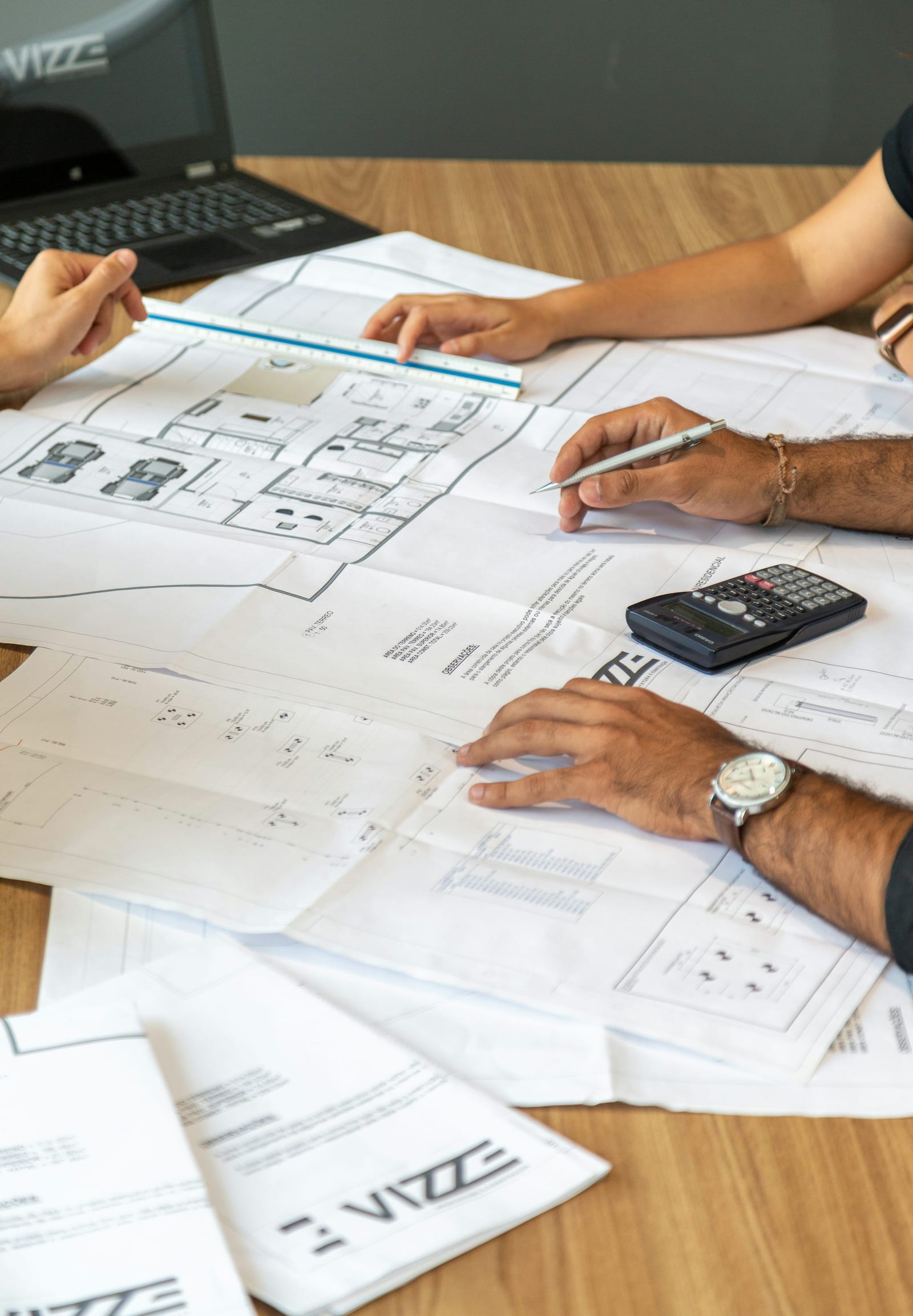 Two people reviewing architectural blueprints and building plans spread across a desk