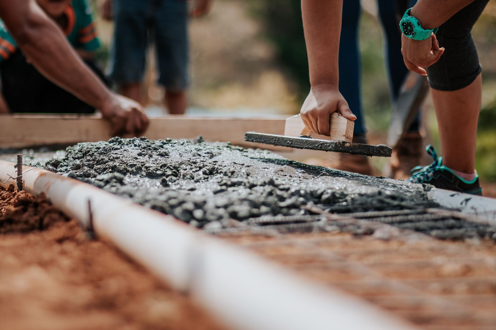 Construction workers leveling fresh concrete at an outdoor site on a bright sunny day